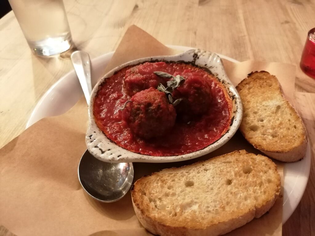 Meatballs in a rich tomato sauce on a plate with two thin slices of lightly toasted bread