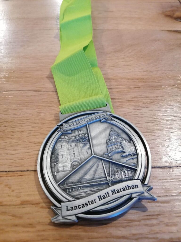 The Great Lancaster Half Marathon medal with a light green strap and engraved with key Lancaster landmarks.